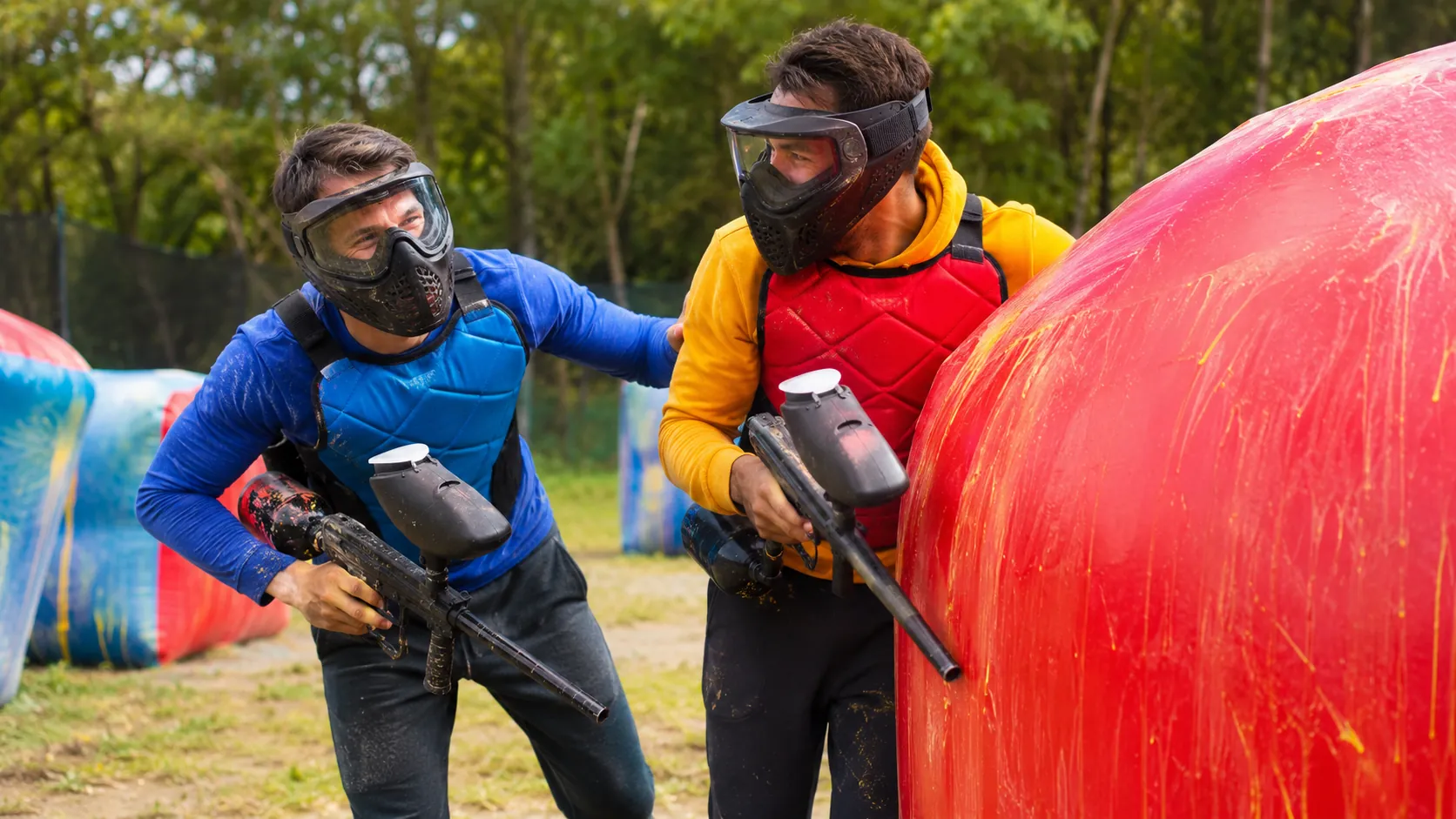 Deux adultes équipés jouent au paintball loisir derrière un obstacle coloré à Neuilly-sur-Marne