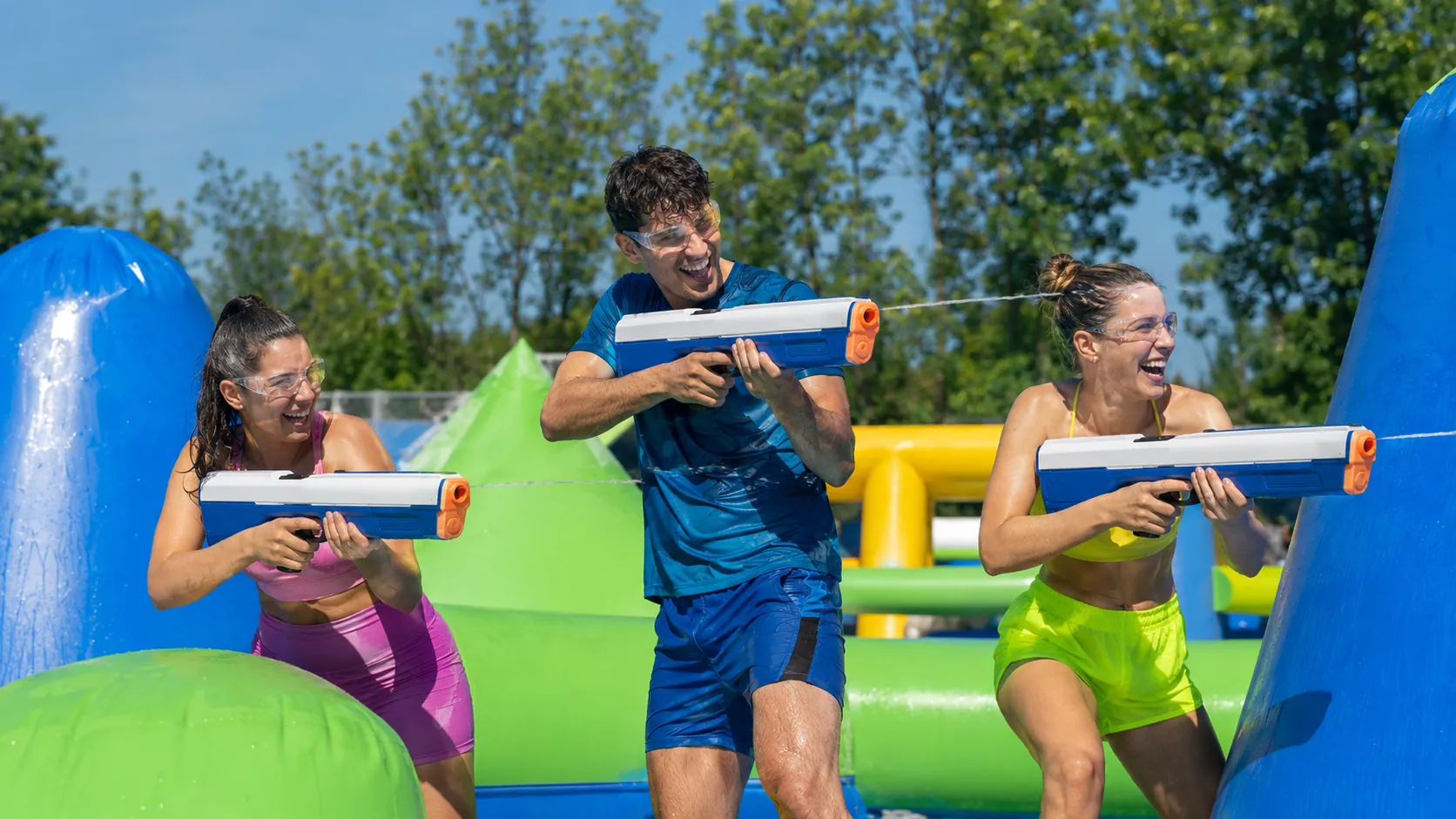 Trois adultes participent à une Water Battle avec des lanceurs électriques sur une arène estivale