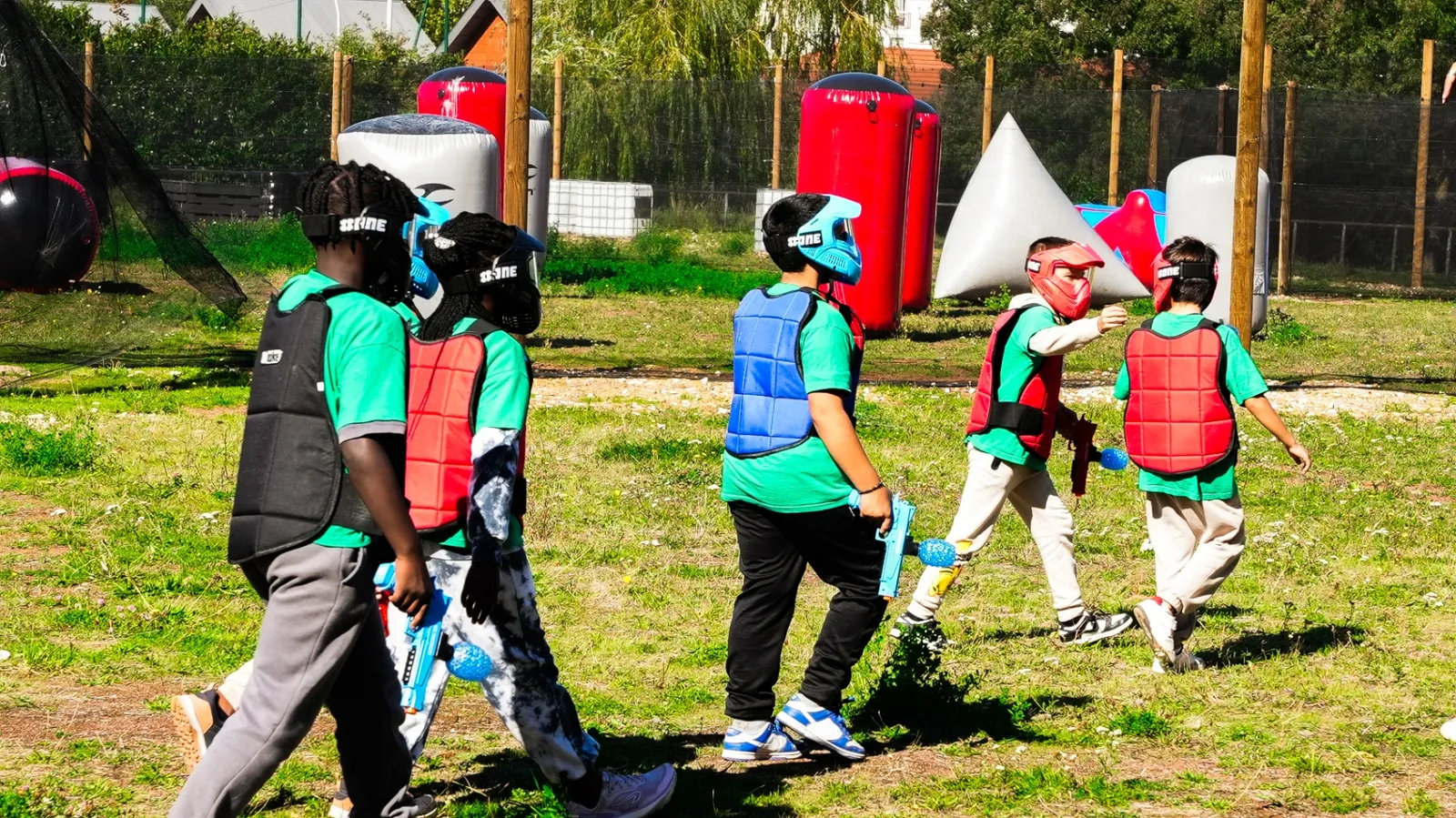 Enfants en partie de Gel Blaster sur terrain airball avec masques et plastrons colorés