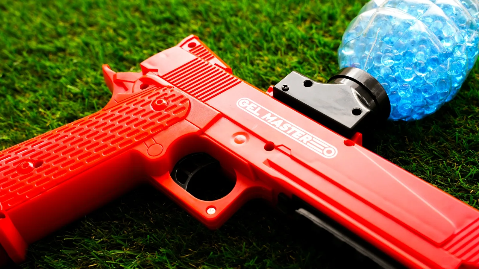 Gros plan d'un lanceur Gel Blaster rouge Gel Master avec billes de gel bleues à NX Paintball
