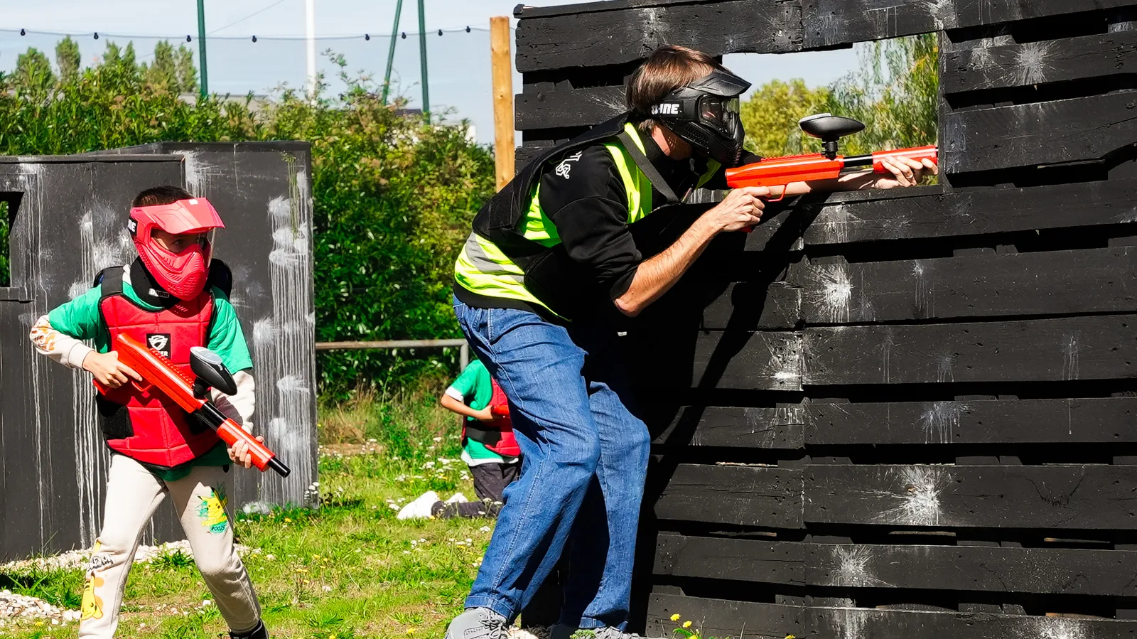 Moniteur et enfant en action derrière une palissade sur terrain paintball outdoor